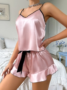 Détail de pyjama en soie rose avec décolleté en V, bordure noire et nœuds en ruban
