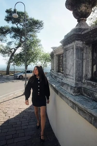 Outdoor shot of a women's black knit set featuring large white buttons and a mini skirt
