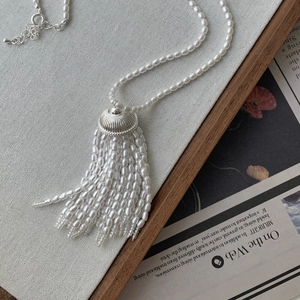 Detailed close-up of pearl fringe tassel necklace with silver textured cap on linen
