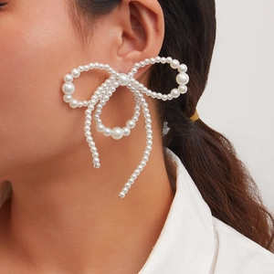 Macro side view of oversized white faux pearl bow earring worn on ear showing detail