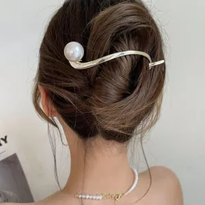 Detailed view of an elegant gold curved hair clip with a large pearl on a French updo