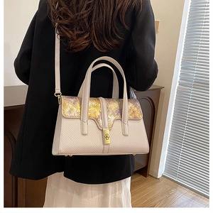Detail of floral embossed flap and golden twist lock on creamy white leather handbag