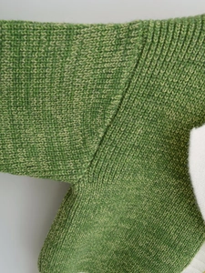 Detailed macro view of green V-neck sweater showing thick knit texture and seam quality