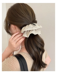 Detail of cream knitted scrunchie with wave lace edge on brown wavy ponytail