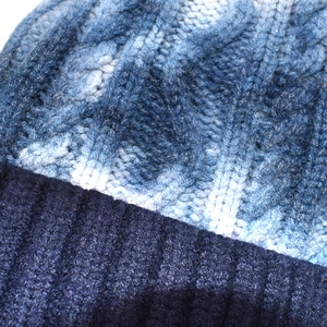 Detailed macro view of cable knit pattern and blue tie-dye gradient on a warm beanie