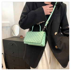 Detail of mint green crossbody bag with M-pattern monogram on a model in a black suit