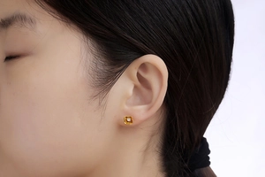 Detailed view of a gold-plated circular stud earring with a central sparkling gemstone