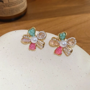 Detail of flower earrings with pink and green crystals and central pearl on ceramic stand