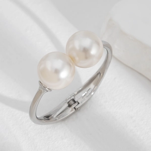 Close-up of a silver open cuff bracelet featuring two polished white pearls on textured background