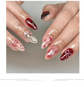 Macro detail of red and cream press-on nails with bow and star patterns in glossy finish