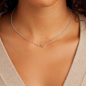 Detail showing a silver double heart necklace worn by a model over a beige knit sweater