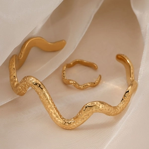 Golden wavy jewelry set with hammered texture bracelet and ring on beige silk background