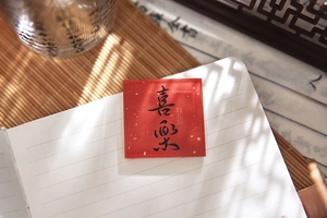 Artistic detail of red acrylic fridge magnet with 'Xi Le' calligraphy on an open notebook
