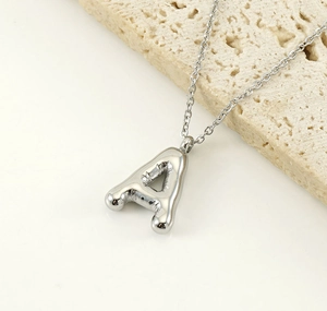 Macro shot of silver balloon style letter A pendant on a natural stone surface