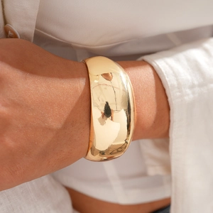 Close-up of a wide polished 18k gold-plated cuff bracelet worn on a female wrist