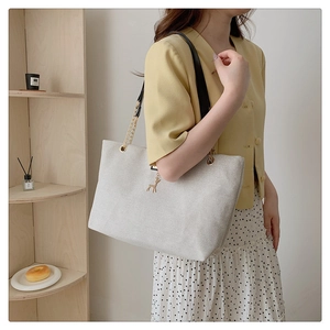 Detail of light grey canvas tote bag with gold deer charm and chain leather shoulder strap