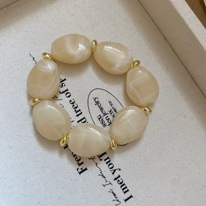 Macro detail of irregular marble-textured acrylic beads and golden spacers on a bracelet
