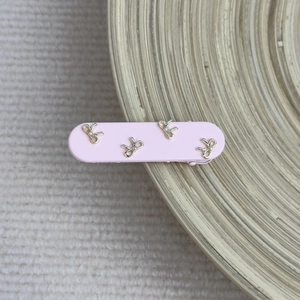 Detail of pink matte hair clip with four delicate golden bows on light wood and knit background