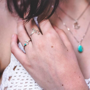 Detailed view of silver rings featuring moon charm and turquoise stone on model fingers