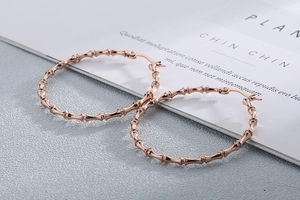 Detailed view of rose gold bamboo texture hoop earrings on a grey textured background