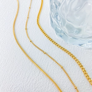Close-up of gold layered chains featuring snake, curb, and bead styles on white background