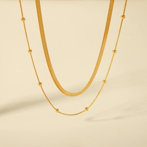 Detailed view of layered gold snake chain and beaded necklace on beige background