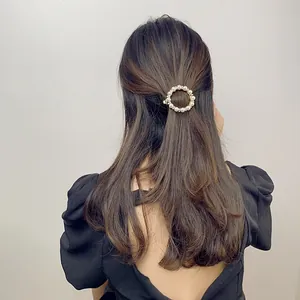 Close-up of circular hair clip with white pearls and rhinestones on gold metal base