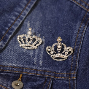 Silver crown brooches with rhinestones and pearls pinned on a denim jacket pocket