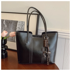 Detail of a black leather tote bag with white stitching and cute cat charm on a wooden table
