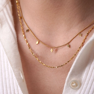 Double-layered gold necklace with diamond star pendants on a model with white knitwear
