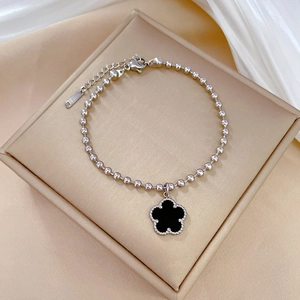 Detailed shot of a silver steel bead bracelet with a black five-leaf clover on satin