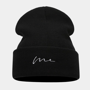 Close-up of black knitted beanie with white me embroidery on folded brim
