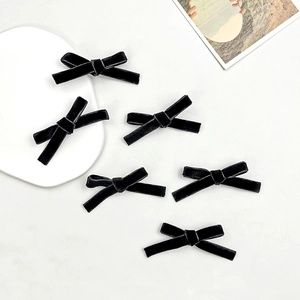 Close-up of six black velvet ballet bows hair clips on a minimalist white tray