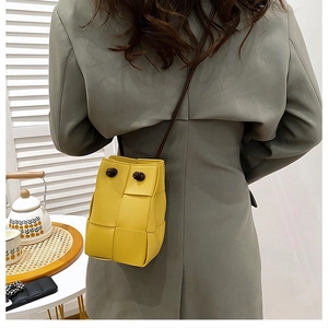 Chic yellow woven bucket bag with slim shoulder strap styled on a grey blazer outfit