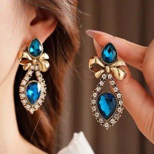 Detail of vintage gold bow earrings with blue teardrop stones and sparkling crystals