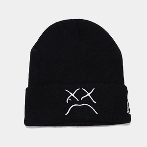 Close-up of black knitted beanie featuring white sad face embroidery and ribbed texture