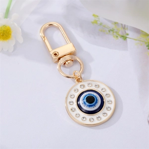 Porte-clés œil bleu en métal doré avec émail et cristaux brillants sur fond blanc épuré