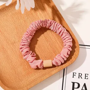 Detailed view of pink pleated satin scrunchie with matte button on a wooden tray