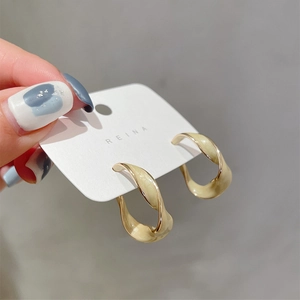 Detail of twisted gold earrings with cream enamel finish held by hand for scale