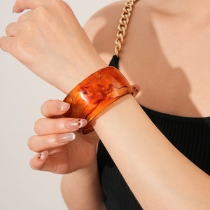 Close-up of a wide amber resin bangle with marble texture on woman's wrist