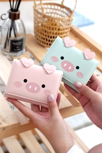 Close-up of cute cartoon pig wallets in pink and mint green held by hand with heart detail