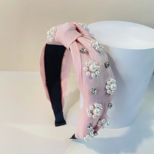Detailaufnahme von rosa geknotetem Stirnband mit weißen Kunstperlen und Strasssteinen