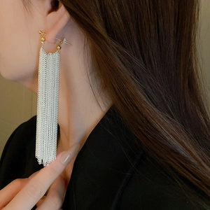 Dramatic long metal chain tassel earrings with golden bead accents worn by model