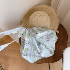 Detail of floral striped canvas tote bag on a rustic wooden table with straw hat