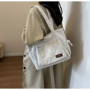 Detail of corduroy tote bag in beige with front zipper pocket and brown leather patch