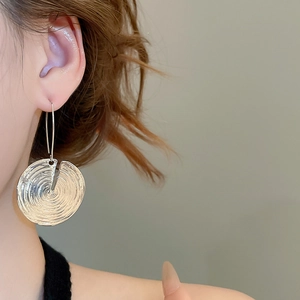 Macro detail of silver round textured earring with concentric lines and unique cut-out design