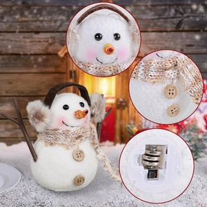 Lighted plush snowman ornament with striped scarf and branch arms in a cozy winter scene