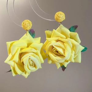 Macro detail of yellow fabric rose earrings with green leaves on acrylic stand