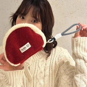 Detail of red plush shell clutch bag with white fleece trim and woven wristlet strap