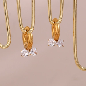 Close-up of golden bow-shaped earrings with two heart-shaped zircons on a display stand